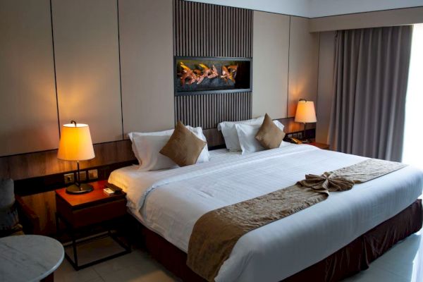 This image shows a modern hotel room with a large bed, bedside tables with lamps, a window with curtains, and a wall decoration above the bed.