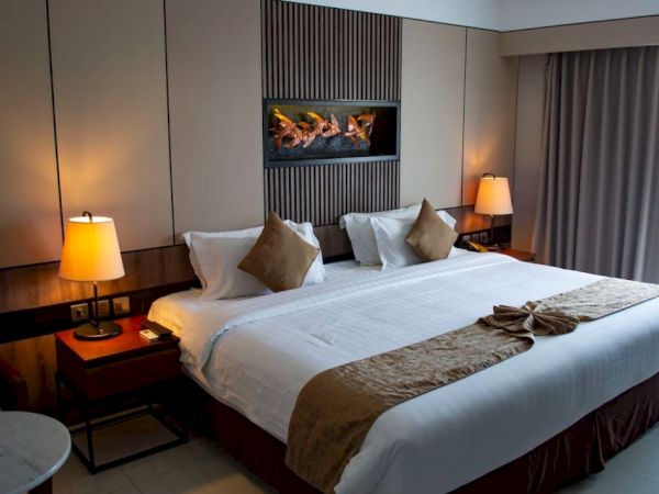 This image shows a modern hotel room with a large bed, bedside tables with lamps, a window with curtains, and a wall decoration above the bed.