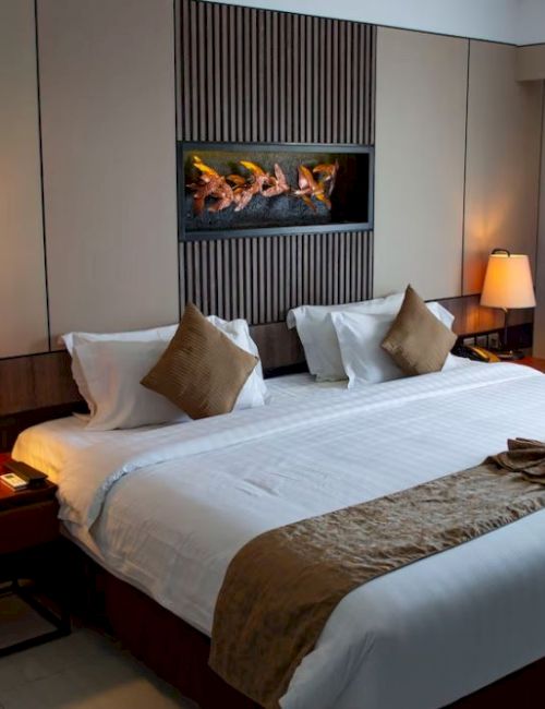 A well-lit hotel room with a large bed, two side tables with lamps, earthy tones, a wall-mounted artwork, and curtains covering a window or door.