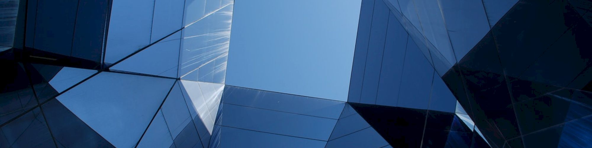 The image shows a modern architectural structure with reflective glass panels and a view of the sky in the middle.