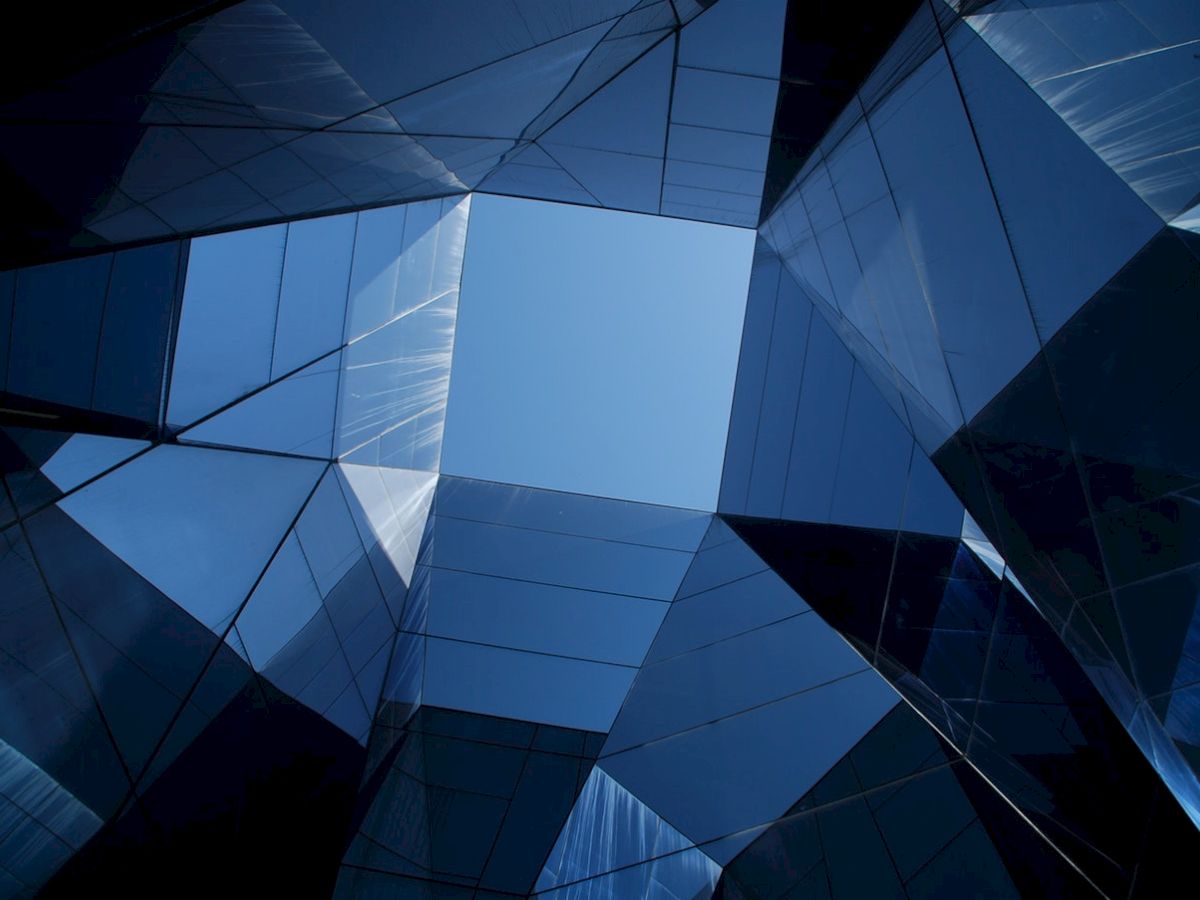 Looking up at a modern glass building with a geometric design and a clear blue sky visible through the center.