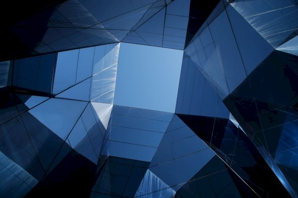 The image shows a geometric pattern created by the reflective surfaces of modern buildings, forming an abstract view looking up at the sky.