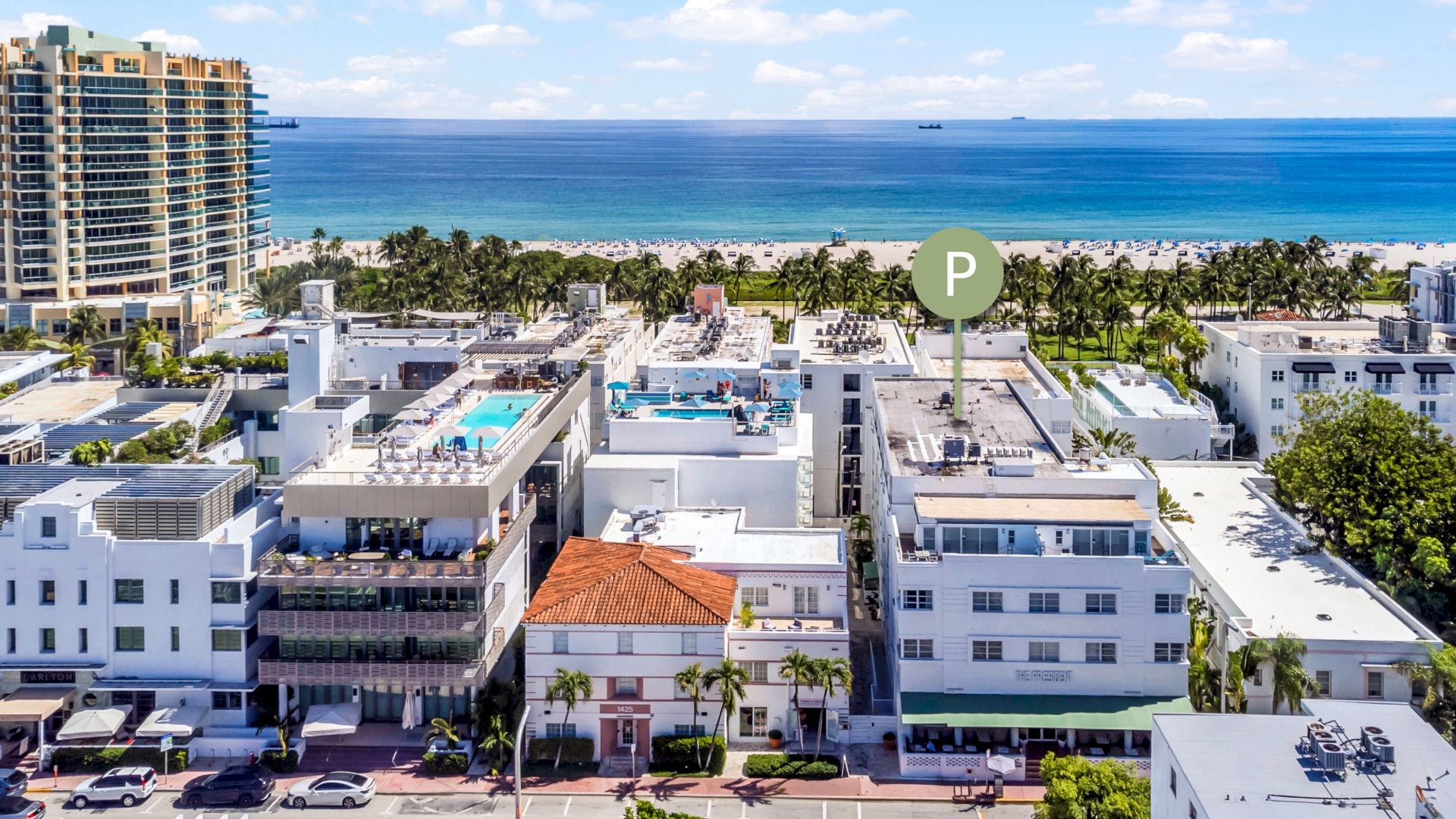 An aerial view of a coastal city with buildings, a few pools, and the ocean in the background under a clear sky.