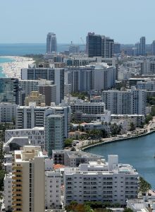 Aerial view of a coastal city with high-rise buildings, a river, and a nearby beach with blue waters and people on the shore ending the sentence.