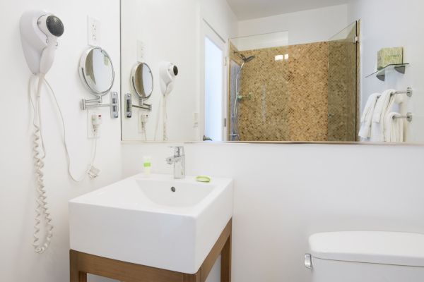 A modern bathroom with a sink, mirror, hairdryer, towel hangers, and shower area enclosed by a glass door. The decor is clean and minimalistic.