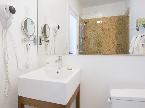 A modern bathroom with a sink, mirror, hairdryer, towel hangers, and shower area enclosed by a glass door. The decor is clean and minimalistic.
