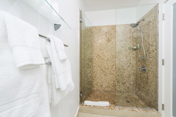 A bathroom with a glass-enclosed shower, tiled walls, white towels on a rack, and a shelf holding folded towels.