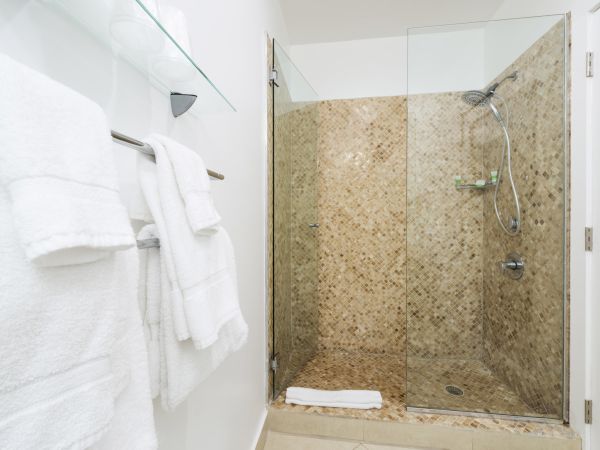 A bathroom with a glass-enclosed shower, tiled walls, white towels on a rack, and a shelf holding folded towels.