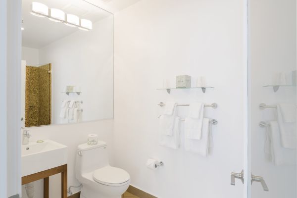 A modern bathroom with a vanity, toilet, large mirror, and shelves with towels and toiletries on a white wall.