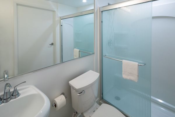 A clean bathroom featuring a sink, toilet, and a shower with a transparent sliding glass door, topped with a small towel on the door handle.