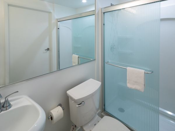 A clean bathroom with a sink, toilet, mirror, and a glass-enclosed shower with a towel hanging on the door.