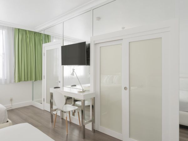 A modern bedroom with green curtains, a wall-mounted TV, a small desk with a chair, and white sliding doors.