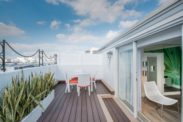 A rooftop terrace with outdoor seating, potted plants, and a sliding door leading to an interior space with modern decor under a partly cloudy sky.