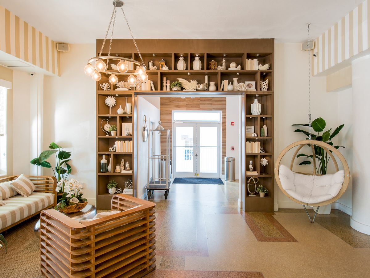 This image shows a well-lit, modern interior with a cozy seating area, a circular hanging chair, plants, and shelves with decorative items.