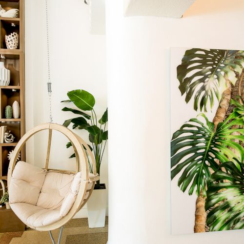 A cozy interior with a hanging chair, tropical plant artwork, and wooden shelves filled with decor items and books.