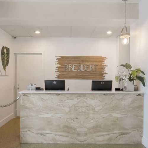 Reception desk in a hotel lobby, with two computers, wall art, and plants, and a sign that says 