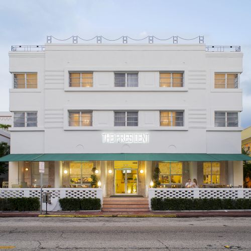 Image of a white, three-story hotel with a neon sign that reads 