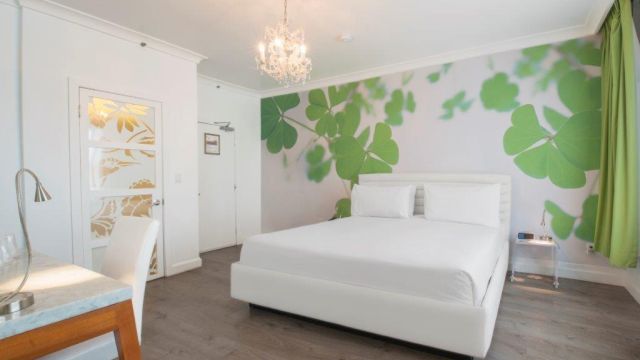 A white bedroom with a large bed, desk, and green clover wallpaper