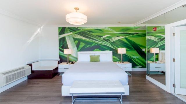 A wide view of a hotel room with a king-sized bed, nightstands, a chaise lounge, and a green accent wall.