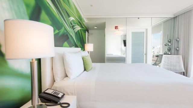 A wide view of a hotel room with a large bed, a lamp, and a mirror.
