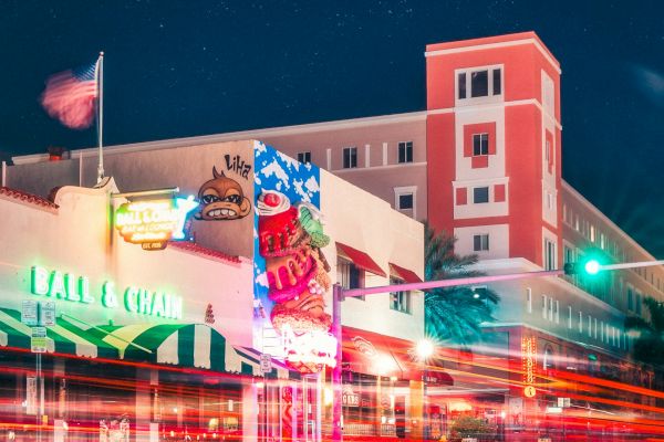 A nighttime street scene with neon signs, a brightly lit building, streaks of light from passing vehicles, and a clear starry sky in the background.