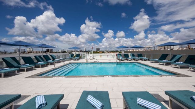 A rooftop pool with lounge chairs and a cloudy sky.