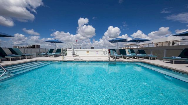 A rectangular pool with blue water and lounge chairs under a cloudy sky.