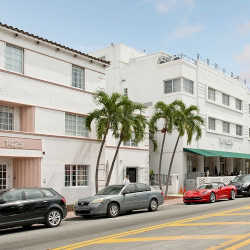 Street view of white buildings with palm trees in front, cars parked along the road, and a large awning over an entrance area.