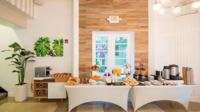 A breakfast buffet with pastries and beverages set on a white table in a brightly lit room with a window.