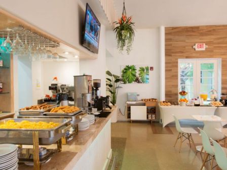 A bright, modern dining area with a buffet setup featuring breakfast foods, a coffee station, and a bar with various beverages.