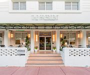 Exterior courtyard of a modern building with patio seating under green awnings, and the sign “THE RESIDENT” above the entrance.