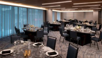 The image shows an elegantly set dining area with round tables, chairs, and dim lighting, creating a sophisticated atmosphere.