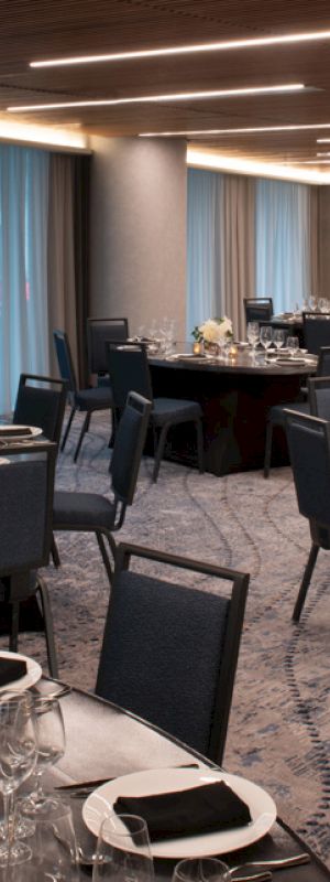 The image shows a modern event venue with round tables set for dining, featuring elegant table settings, decorative centerpieces, and comfortable chairs.