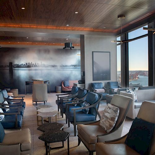 A modern lounge with comfortable seating, a mural, large windows showcasing a view of the water, and a Ferris wheel in the distance.