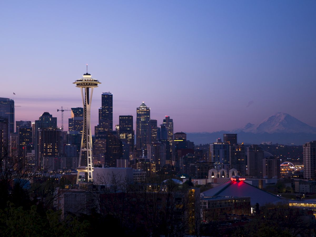 The image depicts a cityscape at dusk featuring a prominent tall tower, modern buildings, and a mountain in the background.