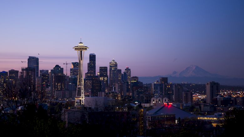 The image depicts a cityscape at dusk featuring a prominent tall tower, modern buildings, and a mountain in the background.